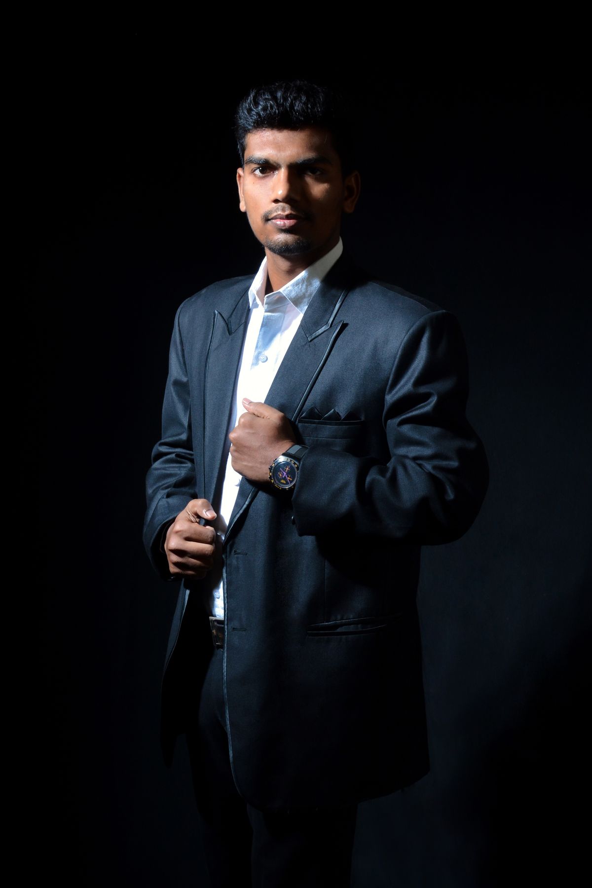 Man in a dark suit photographed against black.