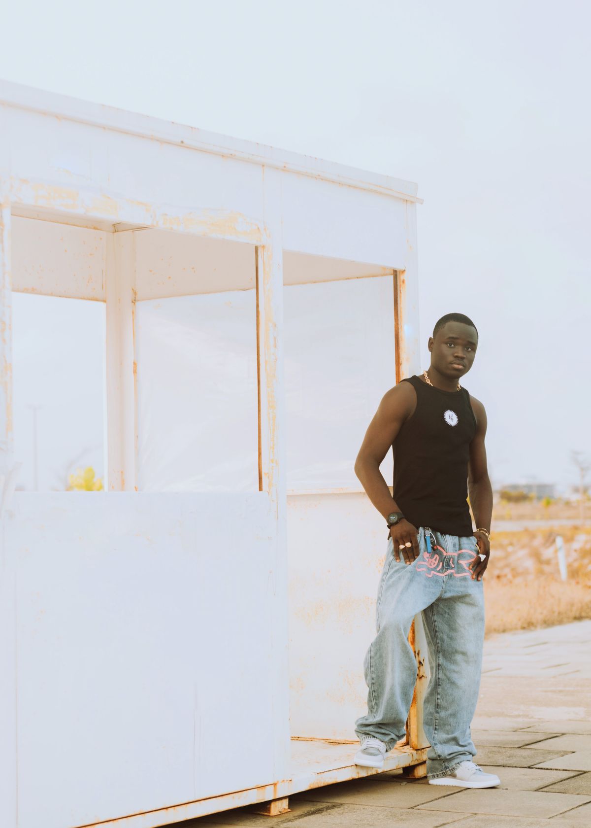 Man wearing a black tank top and loose denim outside.